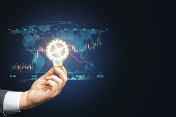 Close up of businessman hand holding lamp with glowing cogwheel with map, forex chart and mock up place on blue background. Conceptual skills, trade and technology concept.