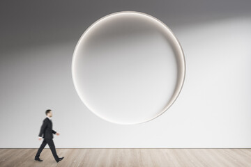 Obraz premium Businessman walking in minimalistic concrete and wooden interior with abstract clean round frame on wall. Mock up. Exhibition, gallery and art concept.