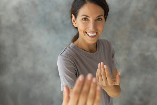 Picture of funny playful pretty brunette woman pretending boxing, inviting to attack her showing hand gestures, standing against grey studio wall with cheerful, laughing face expression