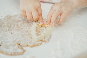 Partially blurred hands of little girl cut out Christmas tree gingerbread cookies from rolled dough in white kitchen