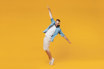 Fototapeta na wymiar Full body young smiling happy man 20s wearing blue shirt white t-shirt stand on toes leaning back fooling around dance isolated on plain yellow background studio portrait. People lifestyle concept