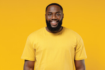 Young smiling happy cheerful satisfied positive fun cool black man 20s wearing bright casual t-shirt looking camera isolated on plain yellow color background studio portrait. People lifestyle concept.