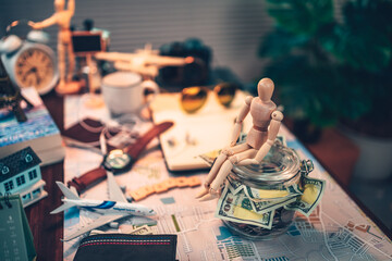 Fototapeta na wymiar Wood human doll sitting on Saving money in glass jar for travel, holiday, vocation on road map on the table. Travel budget concept.