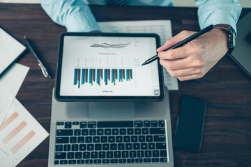 Business hand hold stylus pen touch screen digital tablet with business diagram on the table...