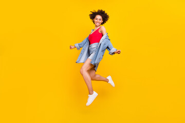 Photo of cheerful dreamy lady jump fly wear denim jacket mini skirt sneakers isolated yellow color...