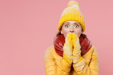 Surprised impressed astonished stupefied young woman 20s years old wears yellow jacket hat mittens looking camera cover mouth with hands isolated on plain pastel light pink background studio portrait.