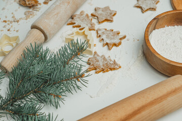 Partially blurred raw gingerbread cookie in shape of christmas trees and stars next to spruce branch, flour, rolling pin