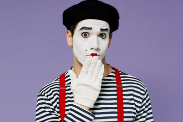 Close up confused preoccupied young mime man with white face mask wears striped shirt beret cover...