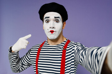 Close up young mime man with white face mask wear striped shirt beret do selfie shot pov on mobile phone point index finger on himself isolated on plain pastel light violet background studio portrait