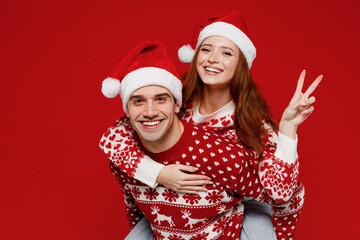 Young cool fun couple friends two man woman 20s in sweater hat giving piggyback ride to joyful, sit...