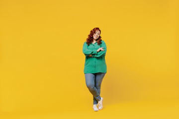 Fototapeta na wymiar Full size body length bright happy vivid fancy young ginger chubby overweight woman 20s wears green shirt looking camera smiling hold hands crossed isolated on plain yellow background studio portrait.