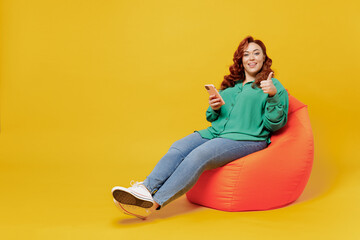 Full size young ginger chubby overweight woman 20s wears green shirt sit in bag chair hold in hand...