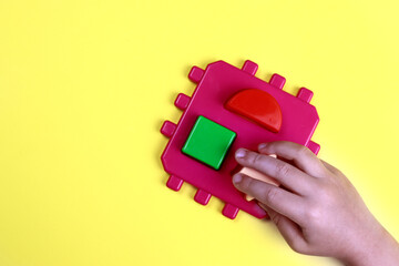 child plays a developmental constructor on a yellow background, hands close-up