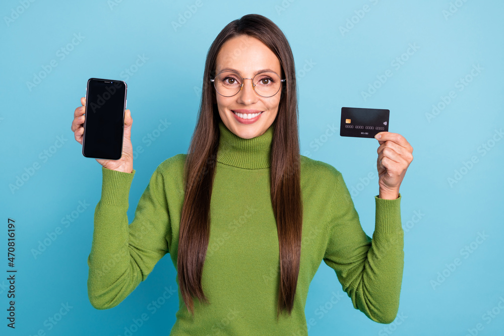 Sticker Photo of shiny cute woman wear green turtleneck glasses holding bank card modern device empty space isolated blue color background