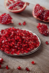 red pomegranate grains and fruit halves on a wooden table vertical frame