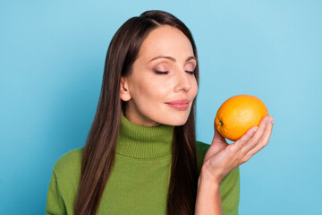 Photo of pretty dreamy mature lady dressed green turtleneck spectacles enjoying orange aroma smiling isolated blue color background