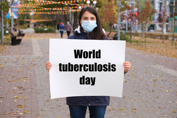 A woman in a medical mask holds a poster with the text World tuberculosis day