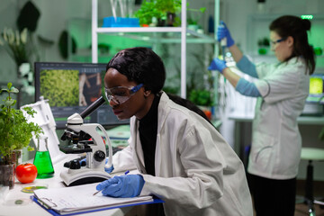 African american biologist scientist analyzing genetic mutation on leaf sample using medical microscope working at biochemistry experiment in microbiology laboratory, Genetically modified plant