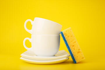 Dishwashing minimal concept. Plates, cups and cleaning sponge against bright yellow background