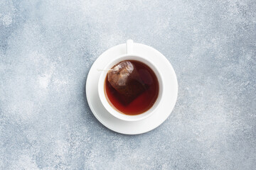 A cup of black tea bags in a white cup with a saucer. Grey concrete background with a copy of the space.