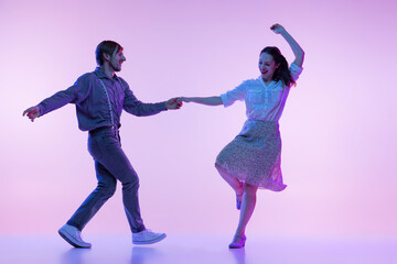 Fototapeta na wymiar Dynamic portrait of young dancers, man and woman in vintage style outfits dancing swing isolated on lilac color background in neon light