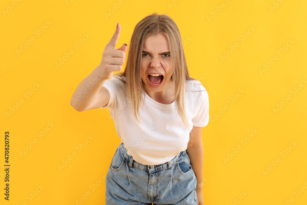 Wall mural Young angry girl in jeans on yellow background