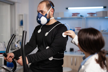 Fototapeta na wymiar Specialist doctor physician putting electrodes sensor on sportman with mask monitoring EGK data in medical examination laboratory. Athlete man running on fintess trainer working at body endurance