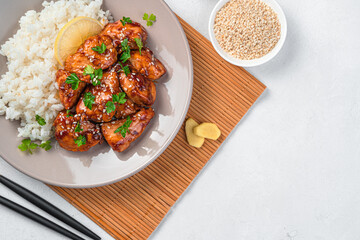 Teriyaki chicken with rice and sesame seeds on a light gray background.