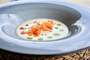 Closeup of cold leek and zucchini soup with salmon, crispy onion and rosemary oil
