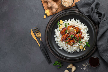 Teriyaki chicken with rice and sesame seeds on a dark background.