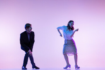 Two young graceful dancers, man and woman in vintage style outfits dancing rock-and-roll isolated on lilac color background in neon light