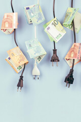 Electric power plugs with Euro banknotes on them hanging on light blue background. Energy...