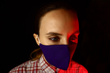 Portrait of a young beautiful woman in a protective mask on a black background in neon light