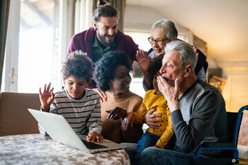 Happy multi-generation family gathering around notebbok and having fun during a video call