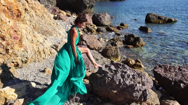 Side view a Young beautiful sensual woman with black hair in a long mint dress posing on a beach with calm sea bokeh lights on sunny day. Girl on the nature on blue sky background. Fashion photo
