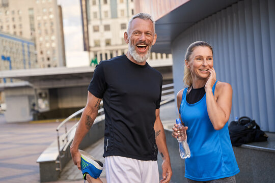 Portrait of happy sportive middle aged couple, man and woman in sportswear smiling, standing together outdoors ready for workout