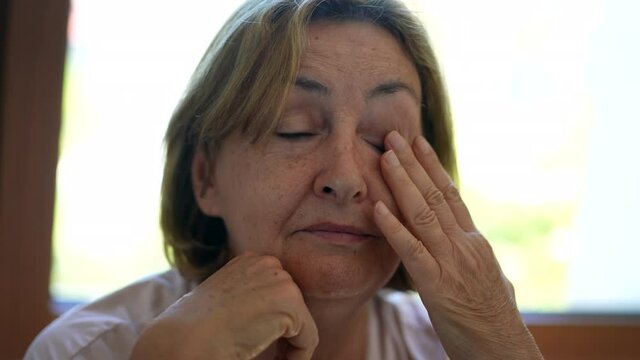 Tired older woman rubbing eye and face. Senior feeling tired
