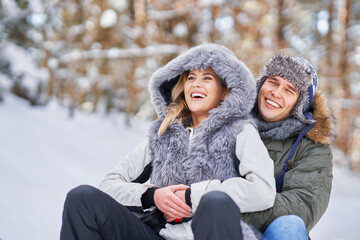 Couple having fun with sledge on snow in winter