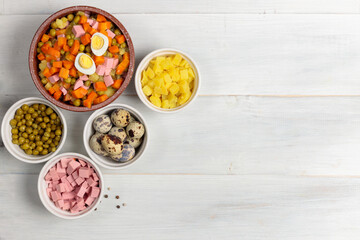 Russian festive salad Olivier in a ceramic bowl and ingredients for cooking. Top view on a light wooden background.
