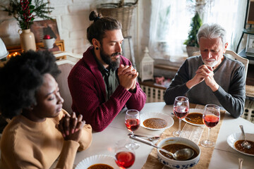 Family and religious concept. Group of multiethnic people with food praying before meal