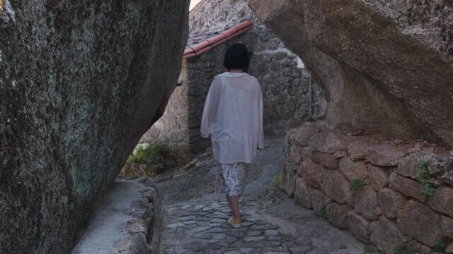 Back view of unrecognizable woman walking between rocky walls of Monsanto historic center, Portugal. Handheld
