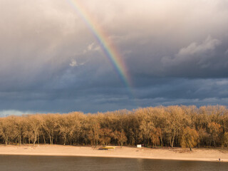 bright rainbow over trees against dark sky