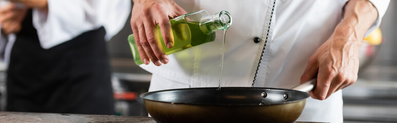 Cropped view of chef pouring olive oil on frying pan in kitchen, banner