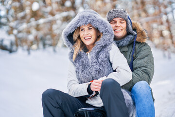 Couple having fun with sledge on snow in winter