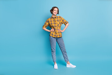 Photo of cheerful pretty lady hands hips wear checkered shirt jeans sneakers isolated blue color background