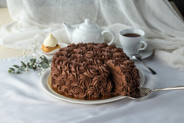 homemade glazed cake and slice decorated with chocolate cream roses and cup of tea on the table