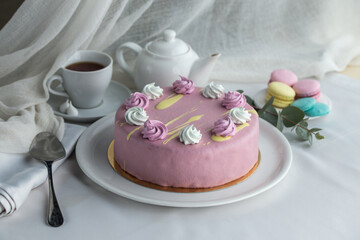Obraz na płótnie Canvas modern mousse cake covered with pink glaze decorated with merinques and cup of tea on the table