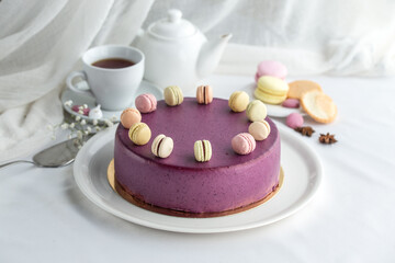 whole cake in violet glaze decorated macaroons and cup of tea on the table