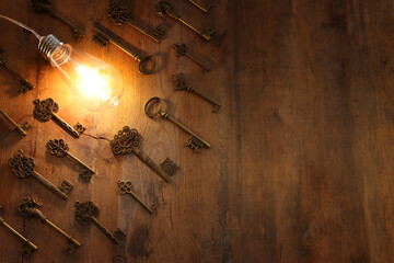 vintage key under bright lightbulb over wooden table. concept of finding the best solution