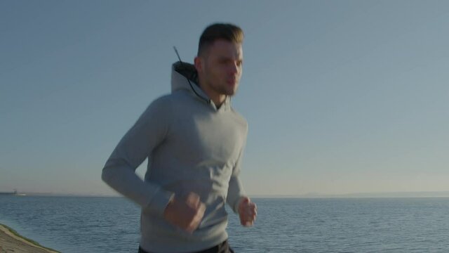 Young slim man is running alone near lake, maintaining healthy lifestyle, staying active and motivated, focused on his self-development and growth, Foreground, Slow motion.